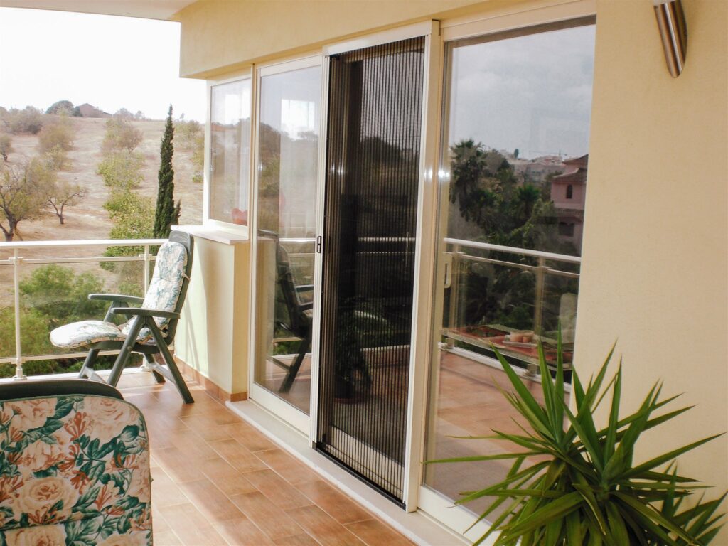 Maison classique couleur crème, avec moustiquaires blanches sur une fenêtre de balcon.