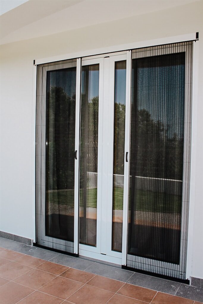 A sliding door with a pleated insect screen, partially opened, allowing a clear view of the garden outside.