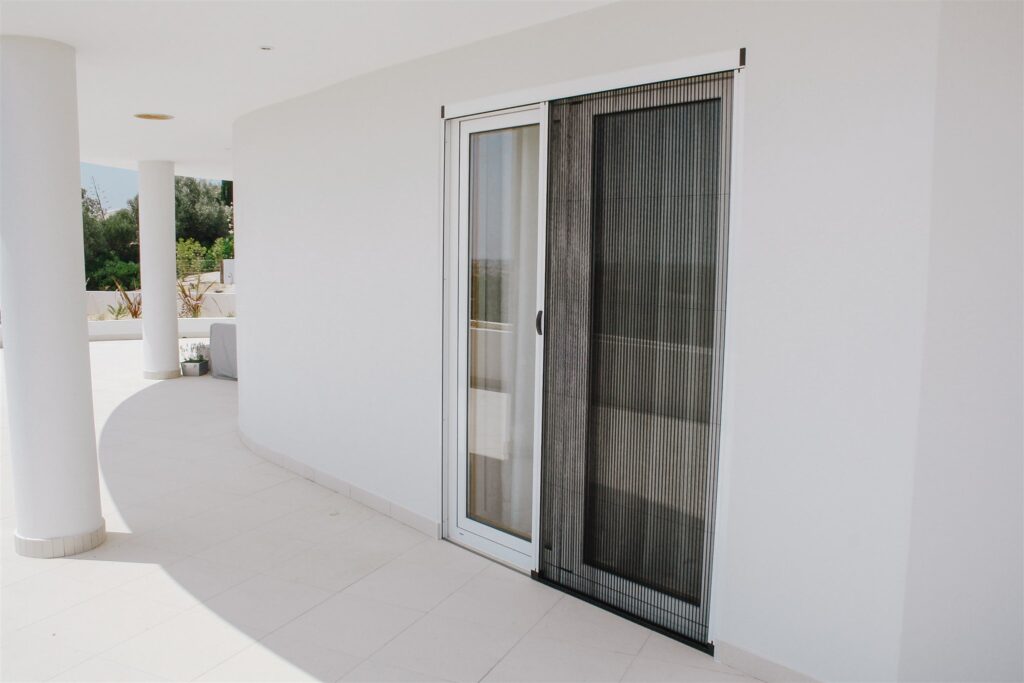 Porte coulissante avec écran plissé anti-insectes Une porte coulissante avec un écran plissé anti-insectes, partiellement ouverte, offrant une vue dégagée sur le jardin extérieur.