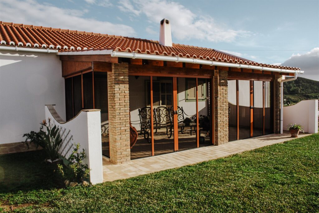 Retractable plisse mosquito screens on sunroom, with wooden frames.