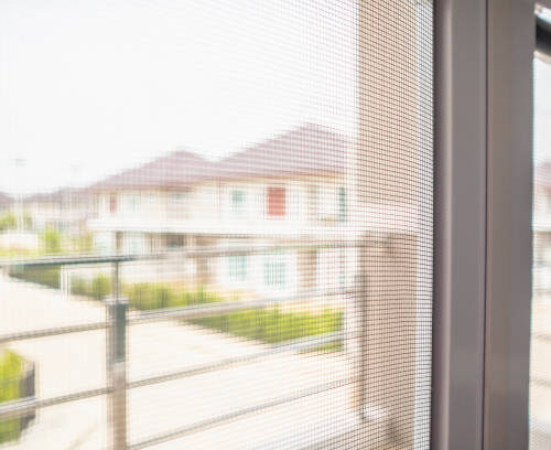 Close-up of a fine mesh insect screen with a view of modern houses in the background.