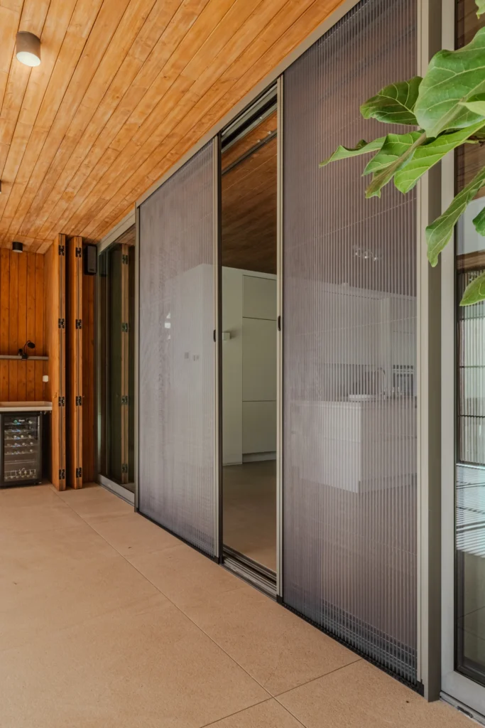 Retractable Plisse mosquito screens on patio doors, featuring a no-trip magnetic track in a modern wooden interior.