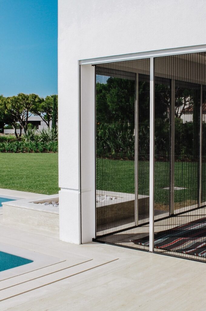 Moustiquaire Plissée Moustiquaire plissée rétractable sur une grande fenêtre avec cadre blanc dans une maison moderne avec une pelouse longue.