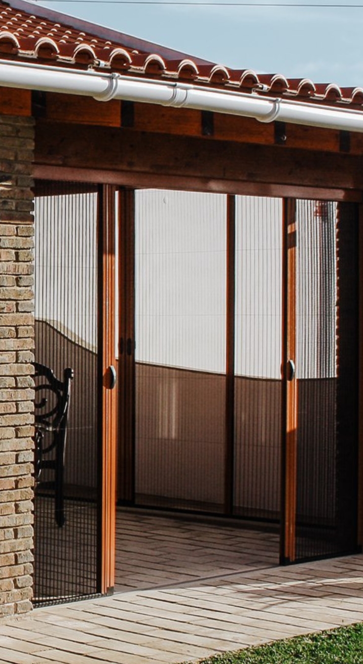 Retractable plisse mosquito screens in sunroom, with wooden frames.